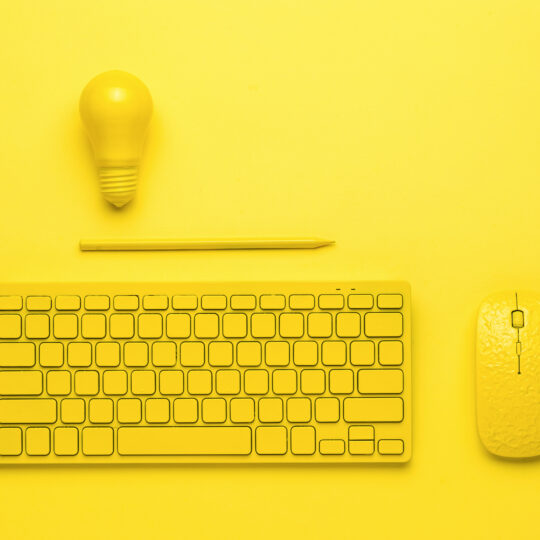 A yellow keyboard with a mouse, a pencil and a light bulb on a yellow background. Monochrome.